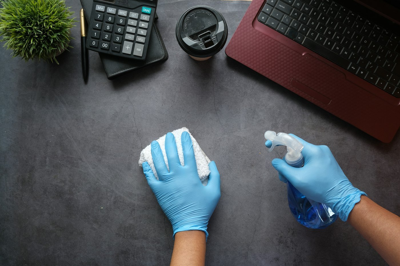 Cleaner in gloves sanitising an office desk