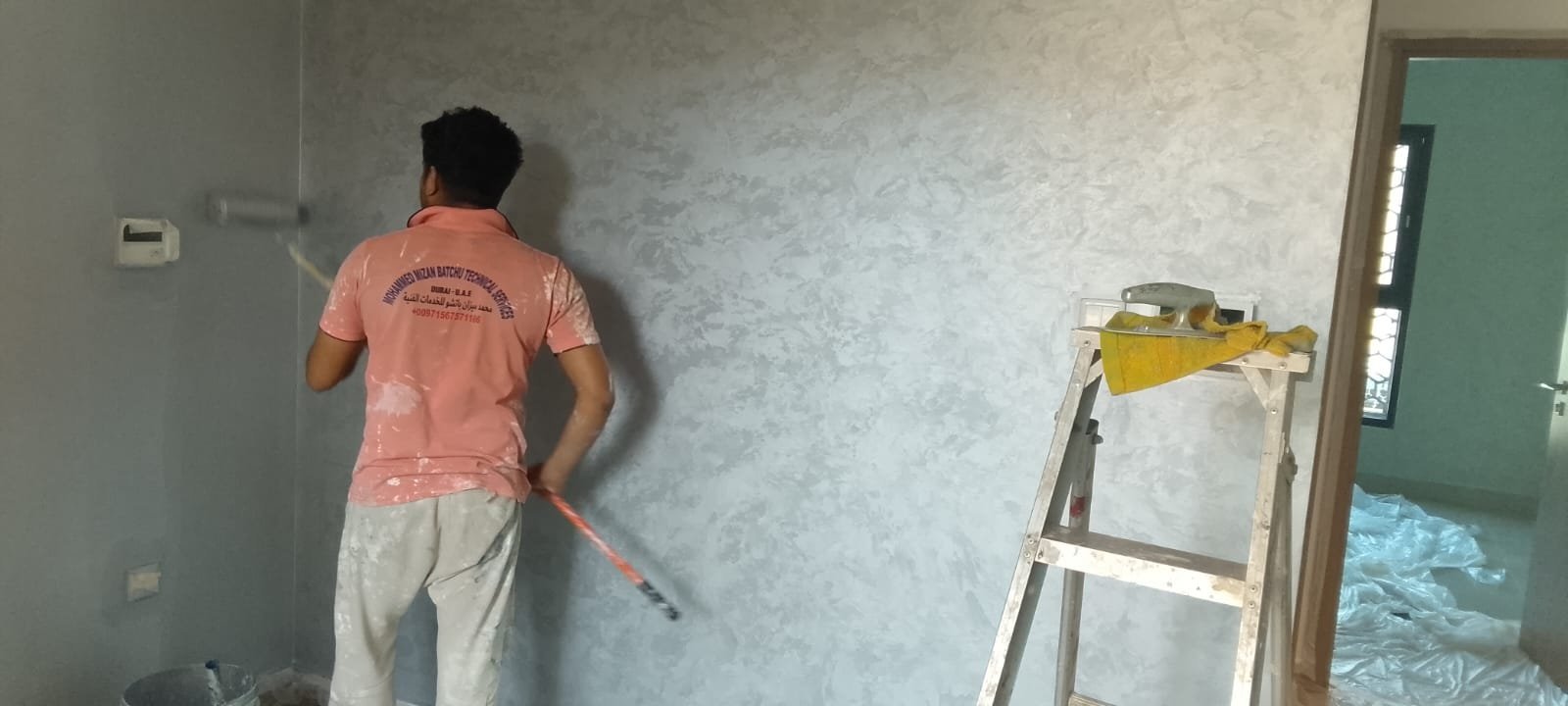 Professional painter in branded uniform applying paint to wall